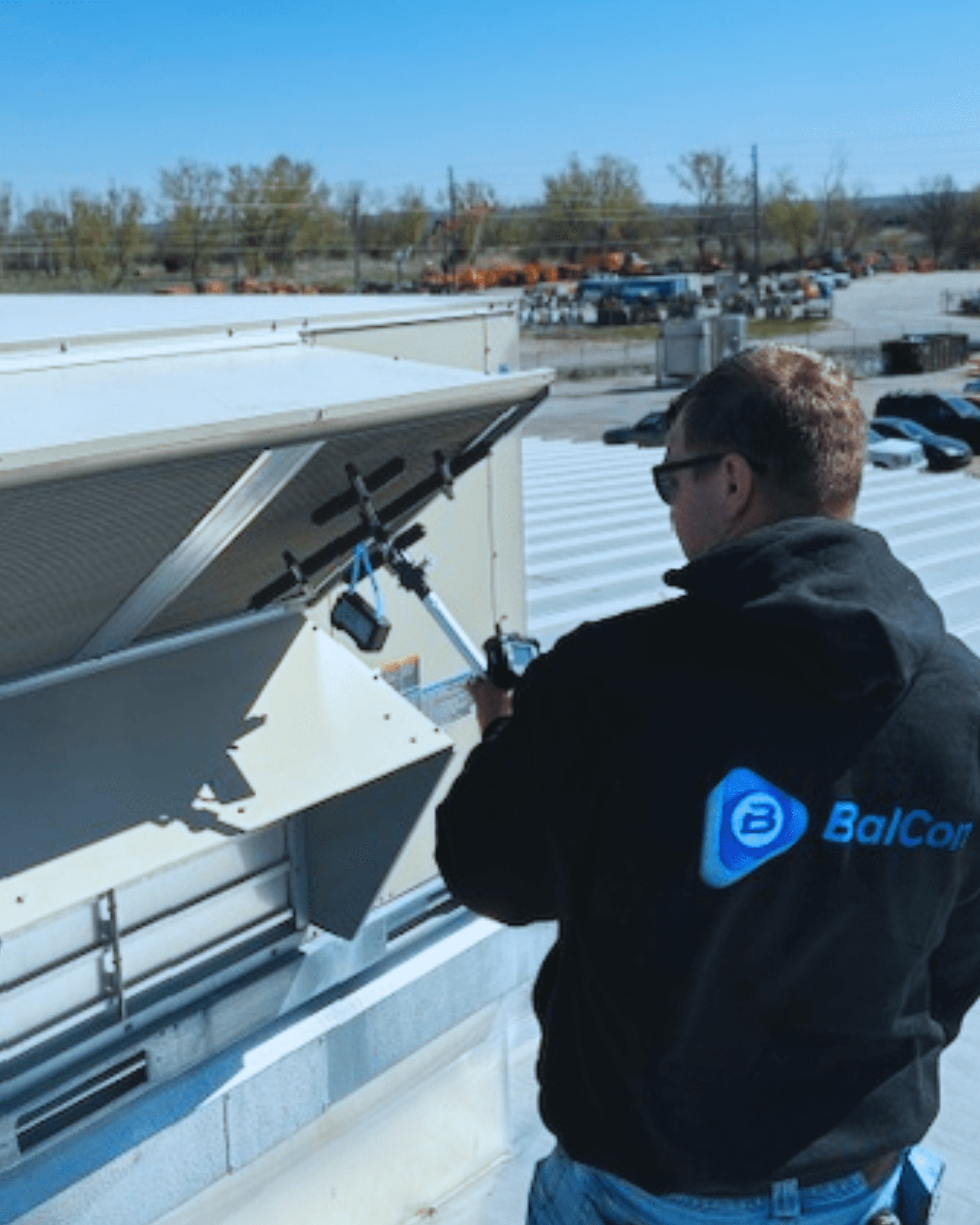Man inspecting rooftop HVAC unit in outdoor setting, wearing a jacket with a logo.